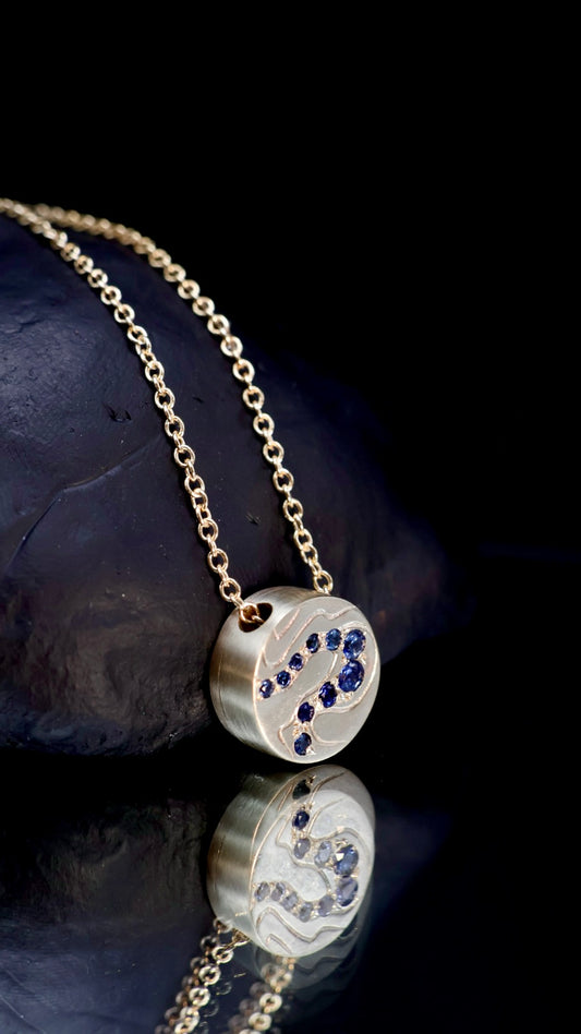15. Robyn Clarke, Birrarung Contour Pendant, 9ct yellow gold cylinder pendant with contour line engraving, set with blue Ceylon sapphires, on a 45cm 9ct yellow gold chain